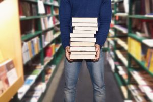 uomo in libreria che acquista libri tenendoli in mano tra corridoio e scaffali